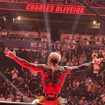 Charles Oliveira sentado en una de las paredes del octagono con los brazos extendidos celebrando su victoria luego de un combate de UFC