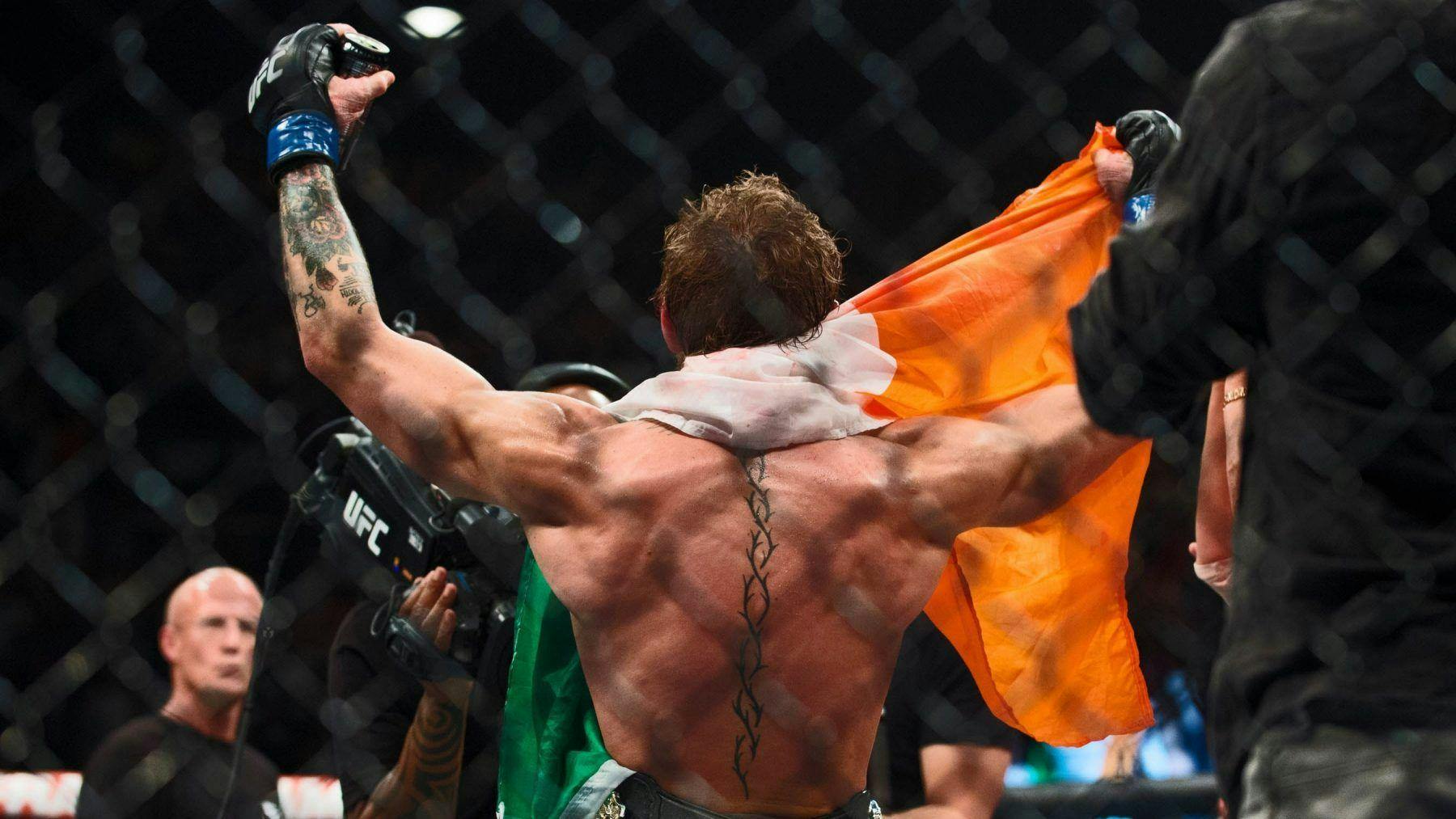 El peleador de mma Conor Mcgregor sosteniendo la bandera de Irlanda con los brazos en alto victorioso después de un combate de ufc