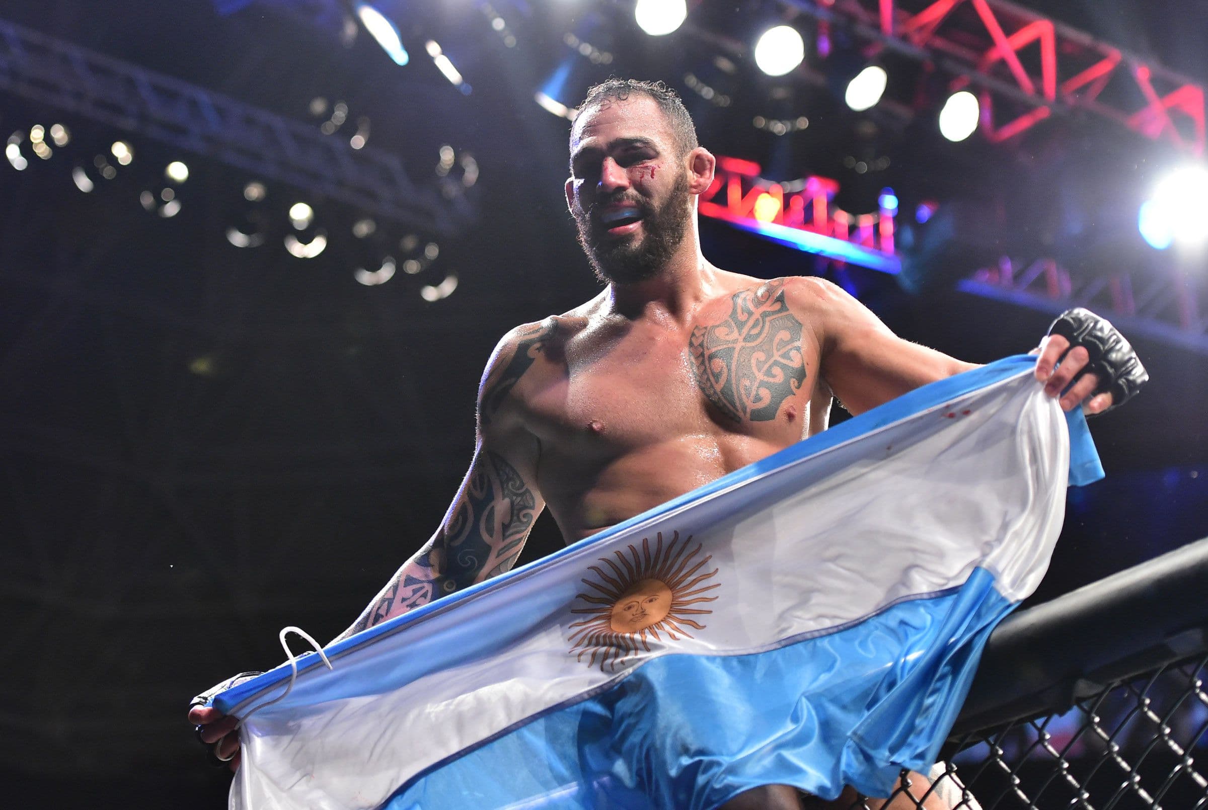 El peleador de mma Santiago Ponzinibbio, sosteniendo la bandera Argentina sentado en la pared de octagono después de un combate de ufc